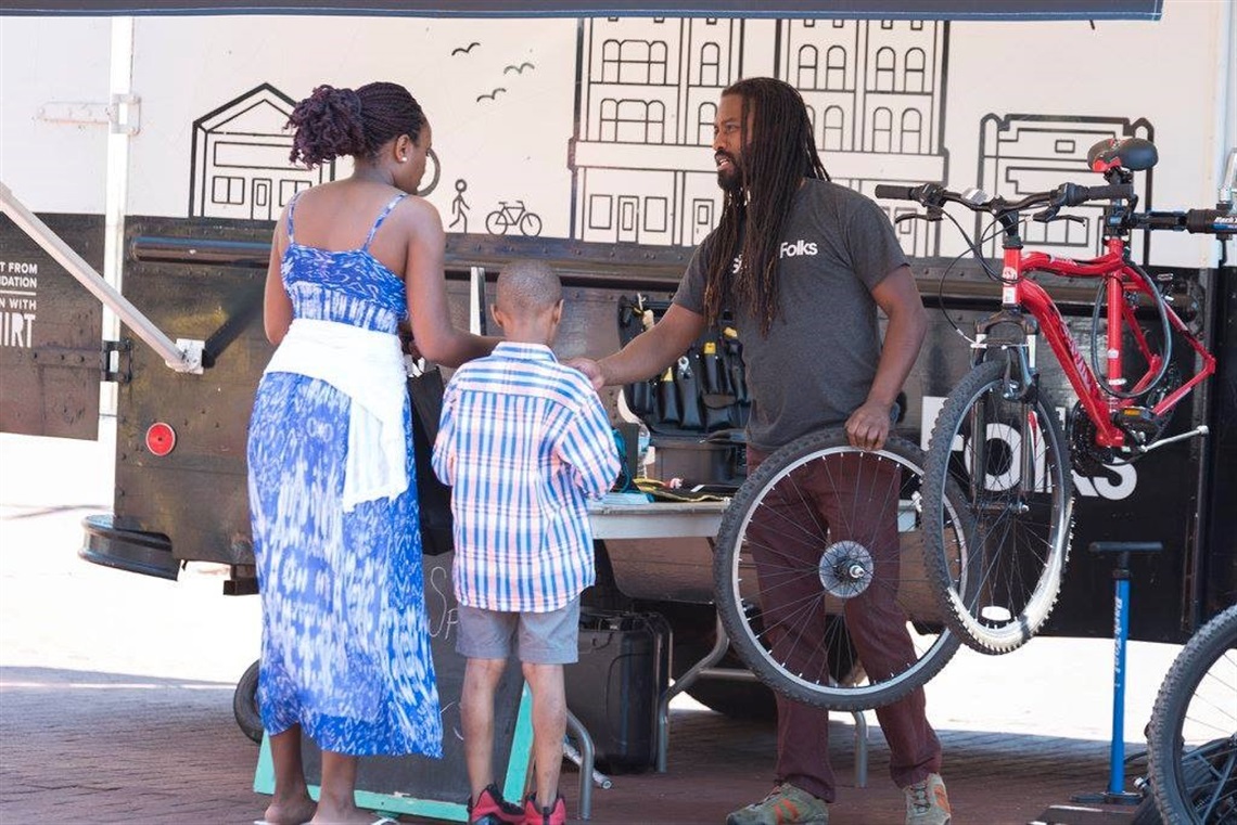 Image of Spoke Folks mobile bike repair station with an employee helping out a mom and son